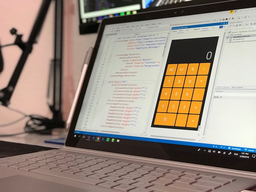A close-up of a laptop displaying a coding editor with lines of HTML and CSS code on the left side and a calculator application with large orange buttons on the right side. The workspace appears to be